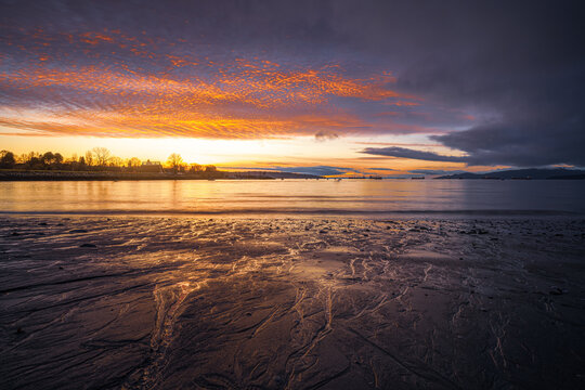 Dramatic sunset sky reflected on wet sand and rocks at low tide, English Bay, Vancouver, British Columbia, Canada