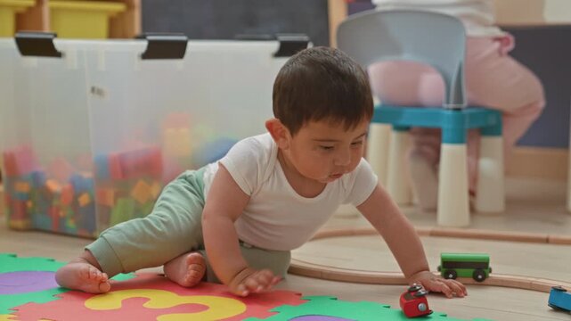 Toddler boy on hands playing with toy car on foam mat and wooden track in building; playful curiosity.
