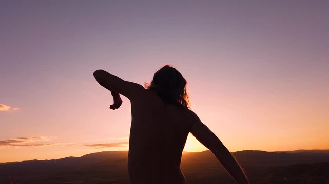 Slow motion rear view of shirtless man with long hair silhouette dancing in mountains during sunset