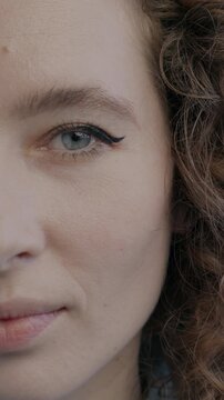 Close-up portrait of confident young lady half face looking at camera with serious expression on black color background. People and emotion concept.