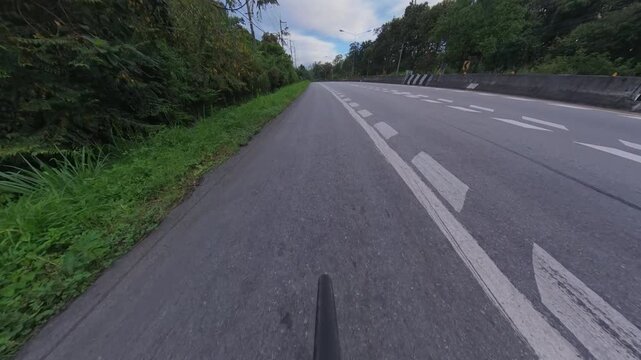 Cyclist POV riding along a winding road through lush green forest, with chevron signs, concrete barriers and marked lanes creating a scenic outdoor cycling route.