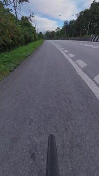 Vertical cyclist POV riding along a winding forest road with clear lane markings, concrete barriers and lush green vegetation on a scenic outdoor cycling route.