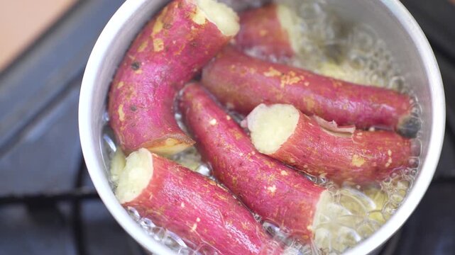 Red-skinned sweet potatoes boiling in a pot of bubbling water on a stove