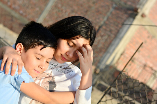 Latin sibling hugging with closed eyes.