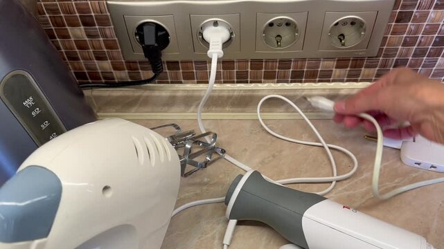 Hand unplugging unused electrical appliances from wall outlets, leaving only needed device connected, reducing electricity consumption and saving energy at home