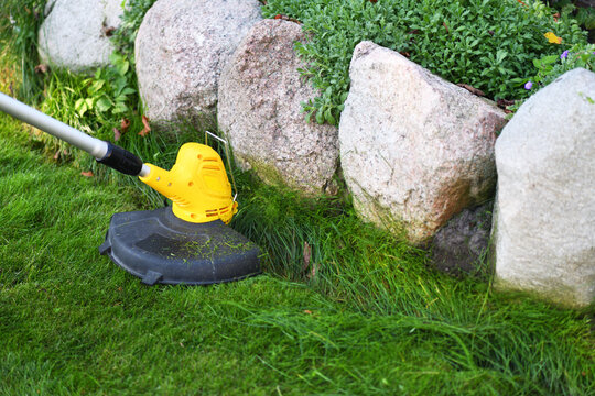 Trimming a green lawn near stones with a string trimmer