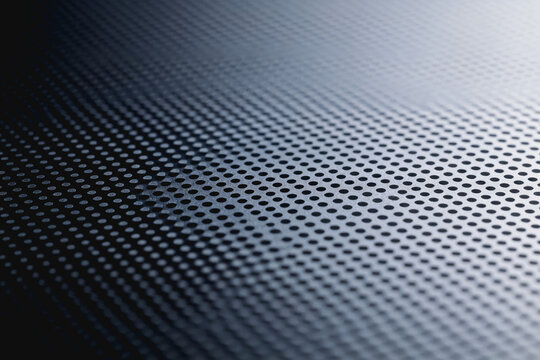 A macro close-up of a perforated metal mesh surface with gradient light and dark tones, showing its structured texture and uniform pattern.