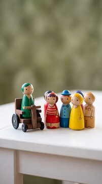 Handcrafted wooden family figures including person in wheelchair by window