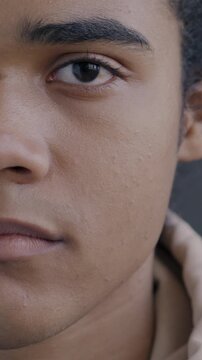 Close-up portrait of African American young man half face looking at camera on black studio background. Person expressing no emotion being serious.