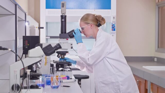 Young female scientist looking through a microscope in a laboratory, conducting biochemical research for medicine and developing new treatments for diseases