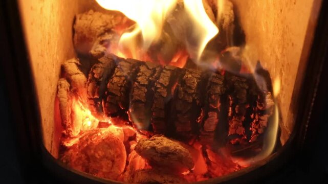 Fire and flames are burning and flickering in a wood stove fireplace with glowing wood logs.
