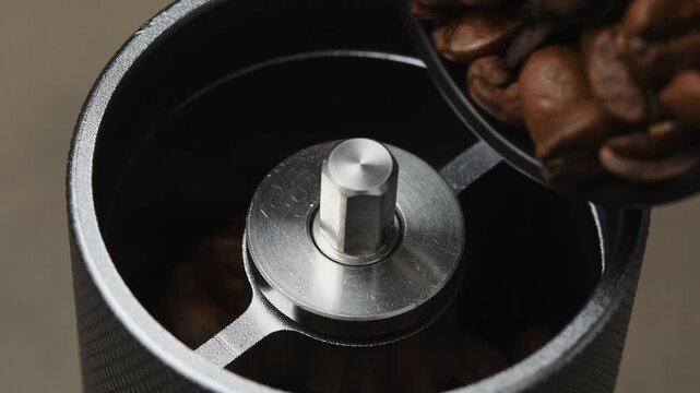 Roasted coffee beans are poured by hand into a manual coffee grinder during beverage preparation.