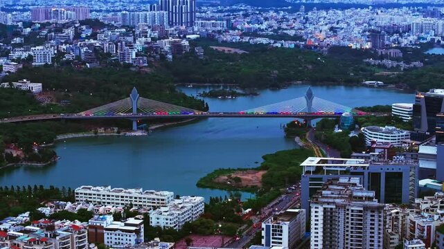 Aerial View of Illuminated Durgam Cheruvu Cable Bridge with apartments, corporate buildings and Ambedkar Open University at hyderabad, telangana, india. evening time, push back shot, drone shot, 4k.