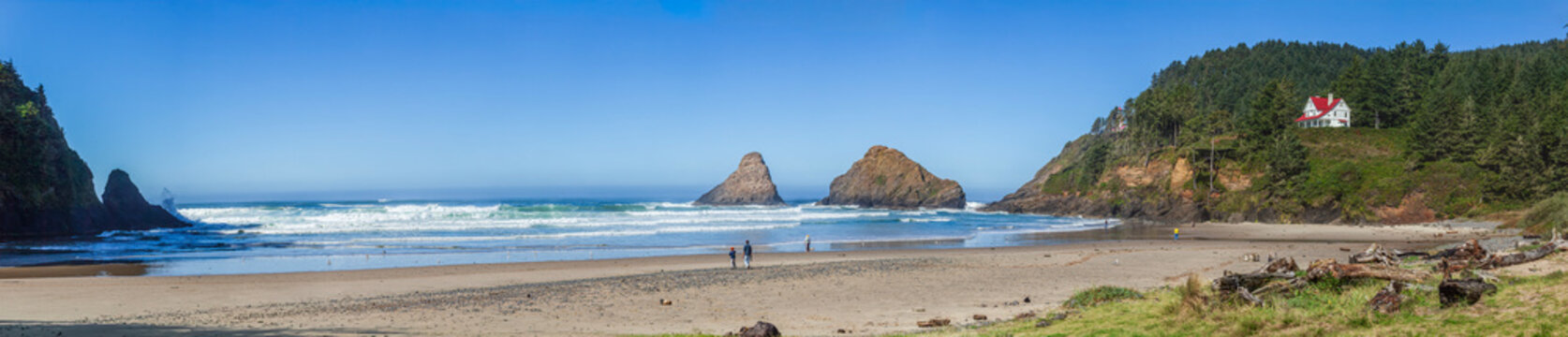 Beautiful wide panoramic view of a sandy ocean beach with green mountains, sea stacks and a historic house