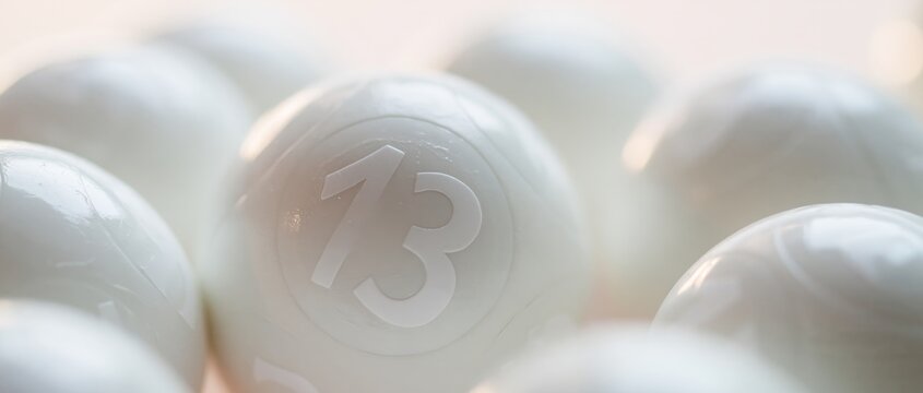 Extreme close-up of a cluster of glossy white lottery balls with the number thirteen prominently displayed in sharp focus, soft directional light catching highlights on smooth curved surfaces against