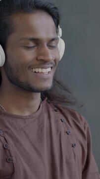 Slow motion of Indian man using headphones listening to music dancing on black background. Person with long hair wearing traditional clothes.