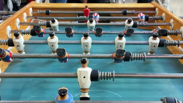 Close up of a wooden foosball table in action, spinning red and white player figures on metal rods during a table football game