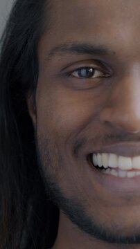 Close-up portrait of happy Indian man half face looking at camera smiling on black background. Individual style and positive emotion concept.