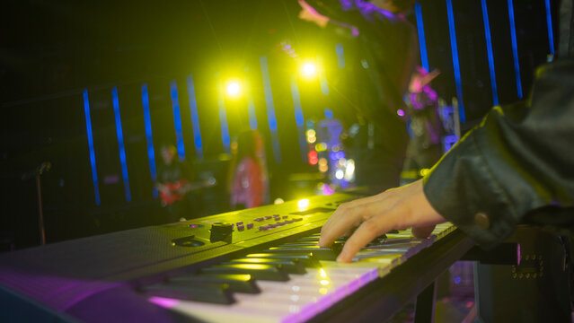Hand of musician playing electronic keyboard on concert stage with copy space