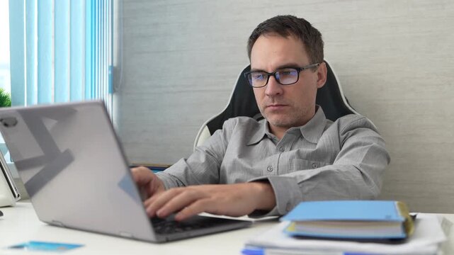 Serious office worker using laptop at desk, focused on online work, business tasks, productivity, and professional responsibilities in a modern workspace.