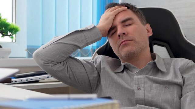 Tired businessman touching his forehead while sitting at his desk, clearly exhausted and bored. Professional burnout, work fatigue, and long office hours.