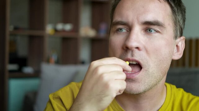Close-up of a man swallowing two medicine capsules, illustrating daily medication, vitamin intake, self-care, and personal health management.