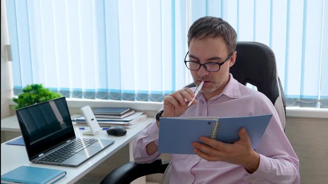 Focused professional taking notes with a pen in a notebook while looking at a computer screen. Business analysis, writing, and active work in the office. the teacher writes the curriculum.