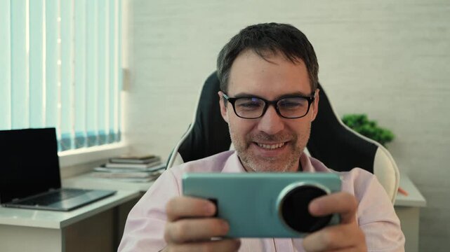 Businessman playing a mobile game on his smartphone during a work break. Office relaxation, digital entertainment, and casual pause.