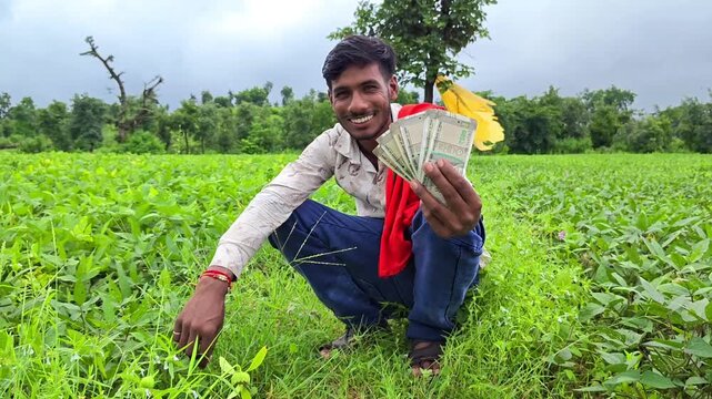 Young farmer sitting in field showing cash to camera. Microfinance and crop profitability concept