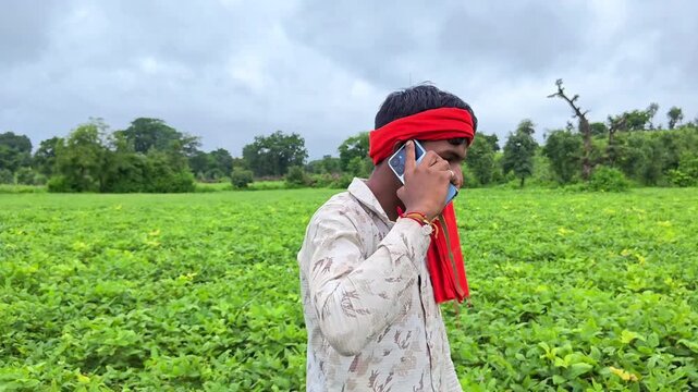 Young indian farmer talking on mobile phone in green agriculture field. Smart farming and digital agriculture concept