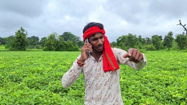 Young indian farmer talking on mobile phone in green agriculture field. Smart farming and digital agriculture concept