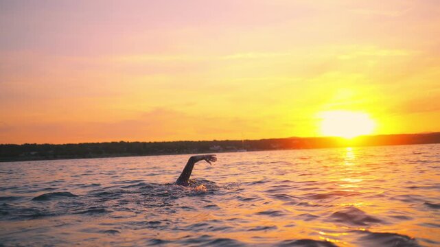 A swimmer battles the waves at sunset, pushing through the water with determination. The tranquil scene represents endurance and perseverance in a serene setting.