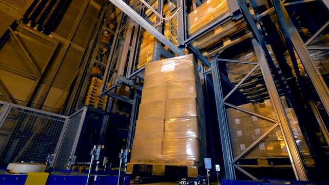 Stacked wrapped cardboard boxes on a pallet being lifted in a warehouse