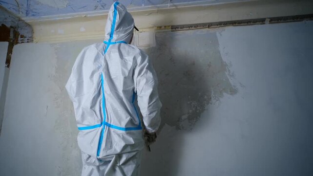 Construction worker wearing a white protective suit applying plaster to a wall with a spatula during a house renovation. Careful and skilled labor for a smooth and perfect finish