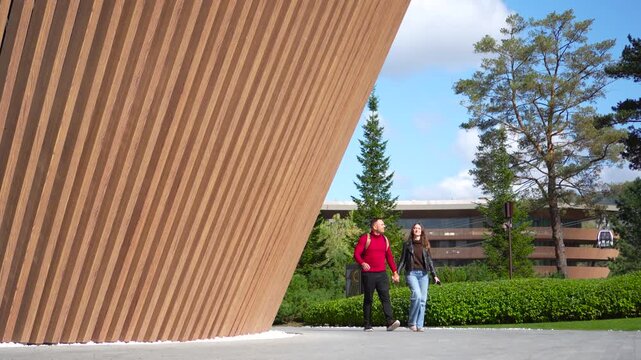 Altai, Russia, 15, September, 2026. Happy romantic couple holding hands and walking outside a luxury resort hotel with a modern wooden parametric facade in a static camera shot