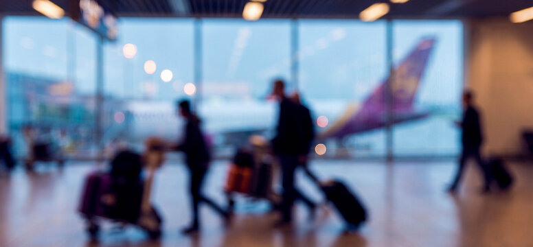 blurred view of travelers in an airport terminal, showcasing people with luggage in motion, emphasizing the hustle and bustle of travel with an airplane in the background.