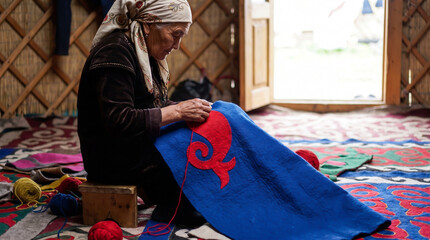 Obraz premium Elderly Woman Embroidering Blue Felt with Red Pattern Inside Yurt