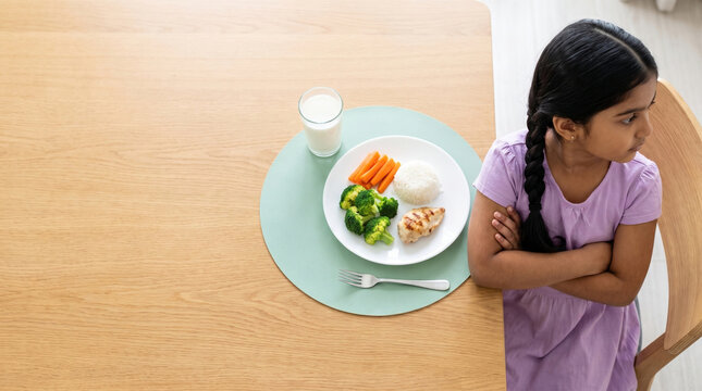 Picky eater girl refusing healthy meal with arms crossed, top view