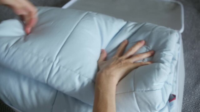 Person folding a clean, light blue comforter and placing it into a transparent storage bag for seasonal bedding organization, zipping it closed for compact and tidy household storage