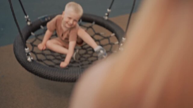 Young boy enjoys swinging on tire swing at outdoor playground moving back and forth with visible delight. scene captures his playful interaction as boy sits in netted seat suspended by ropes