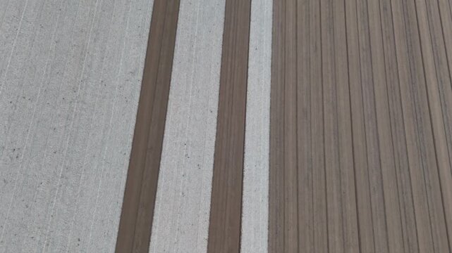 Po Valley agricultural field in Italy showing parallel plowed strips and precise cultivation patterns associated with mechanized farming, top down drone pullback with parallax