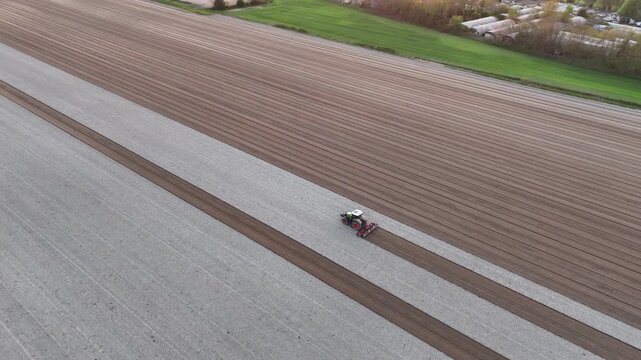 Po Valley agricultural field in Italy with tractor following precise parallel cultivation passes, illustrating mechanized precision farming and digital field guidance, drone orbit parallax