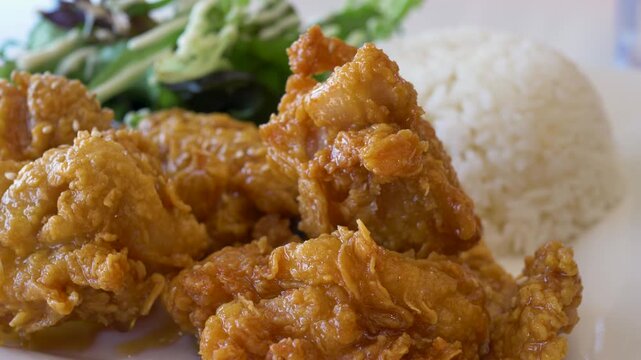 Slow motion close-up of deep fried Korean popcorn chicken pieces with garlic and soy glaze served with a steamed rice and a side salad at an Asian restaurant in Australia food dining and hospitality