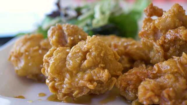 Slow motion close-up of a traditional Korean fried spicy hot popcorn chicken recipe with a garlic spiced glaze served on a dish meal plate with a side salad at an Australian restaurant food and dining