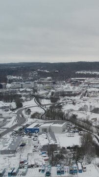 Aerial Drone view showing snow covered commercial area with buildings roads parking lots and surrounding woodland during winter in Storas Angered Gothenburg Sweden