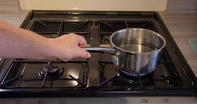 Pan of cold water being put on a Large bottom right gas jet. On a hob in a static caravan