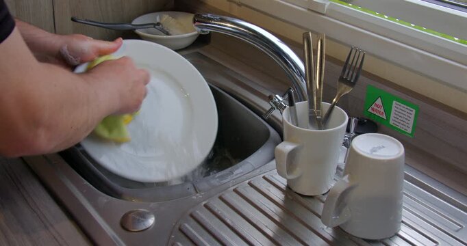 Wide shot of a man washing up at a sink inside a static caravan