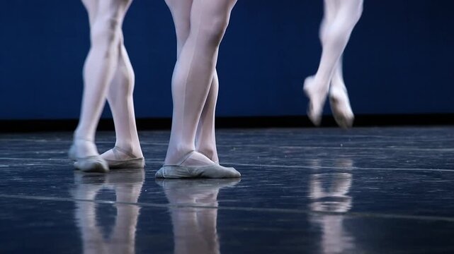 Close-up of male ballet dancers' legs in white tights and soft ballet shoes performing on a reflective dark stage during a classical dance rehearsal.