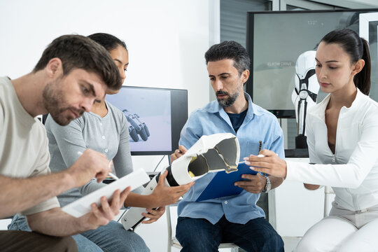 Diverse team meeting in an office to design robotics and test prosthetic limb prototypes, collaborating closely on engineering solutions and sharing ideas for advanced medical technology development.