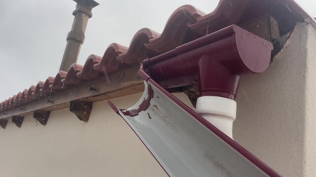 Horizontal view of broken plastic gutter pipe detached from roof edge on house during rainy day causing water leak and needing repair. High quality 4k footage